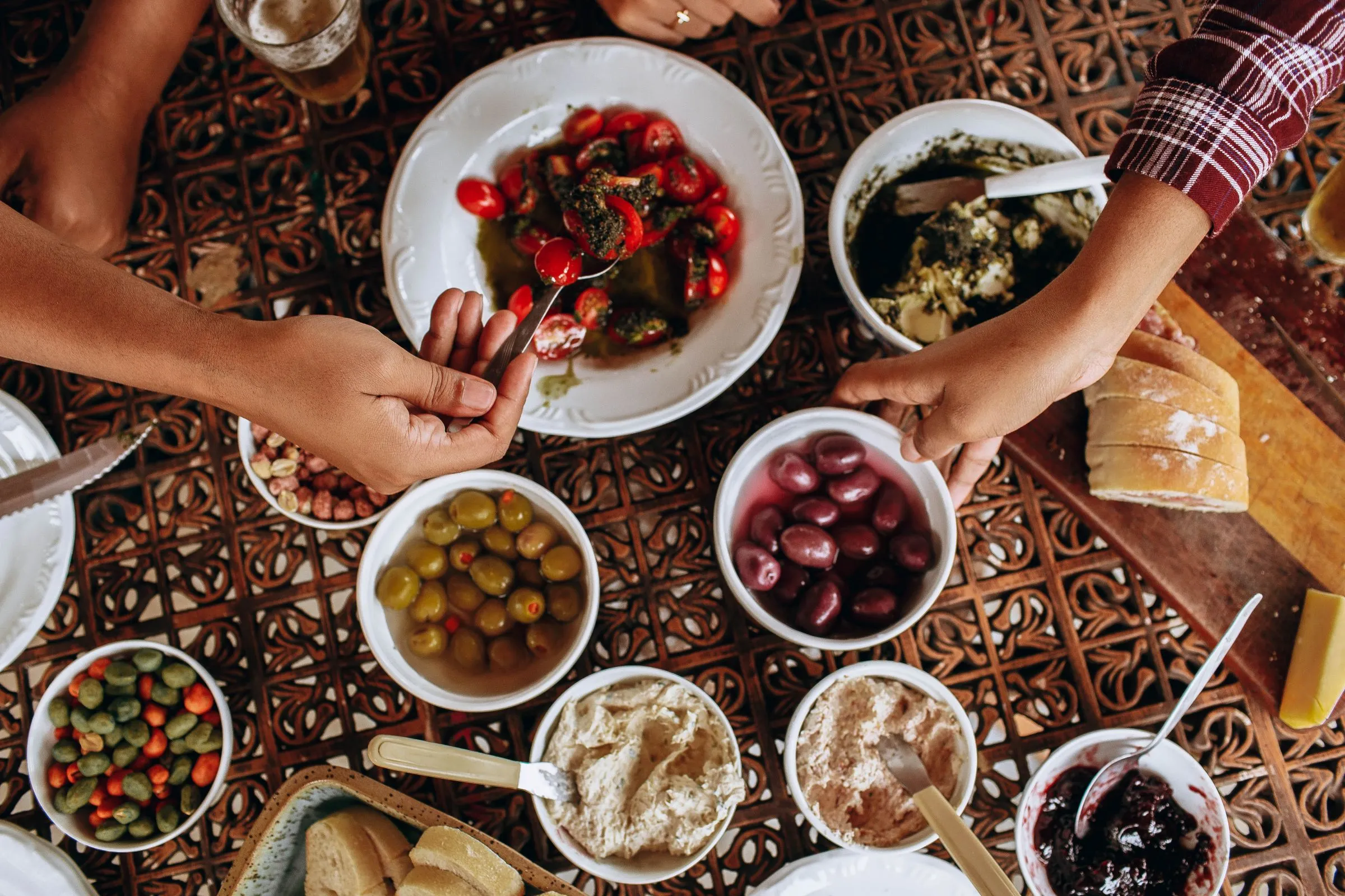 Hands reaching for olives, dips and bread across a shared mezze table.